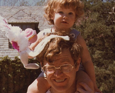 A cropped photo of Charles Koch squinting in the sun with daughter Elizabeth Koch on his shoulders holding an Easter bunny.