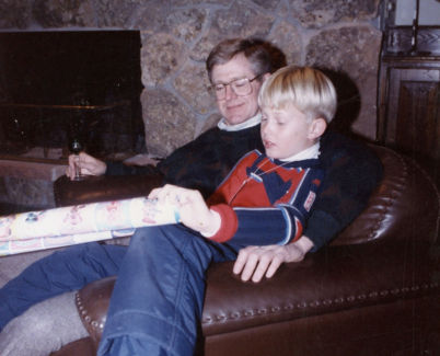 A photo of Charles Koch wearing a sweater and seated in a brown leather chair with son Chase Koch sitting in his lap.
