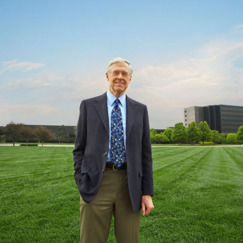 Charles Koch wearing a dark blazer, light blue dress shirt and patterned tie standing on the lawn in front of Koch, Inc.