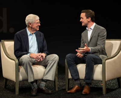 A photo of Charles Koch and Brian Hooks dressed in casual business attire seated on a stage discussing their book.