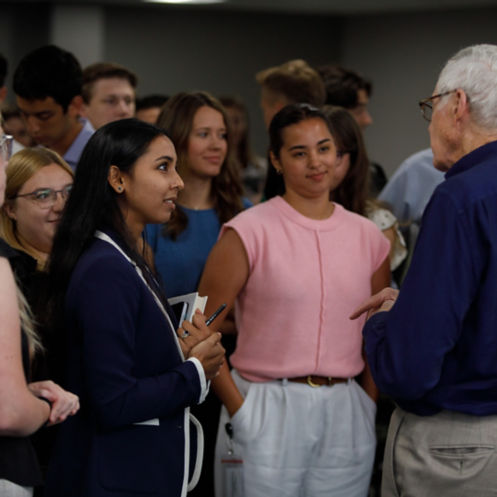 Charles Koch engaging in conversation with a group of summer interns at Koch, Inc. as they listen attentively.