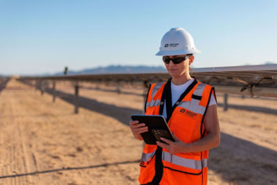 a woman in a hard hat and orange vest holding a tablet