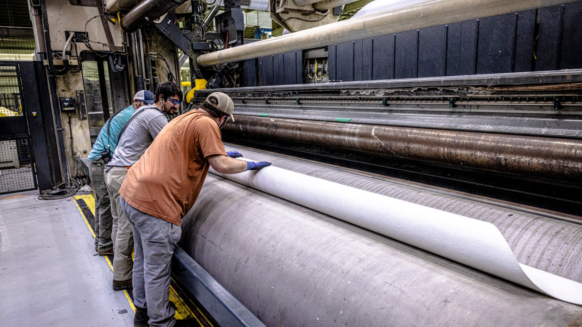 Two men wearing safety equipment are working in a pulp production mill. 