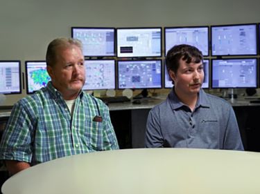 men sitting at a table in front of a computer screen