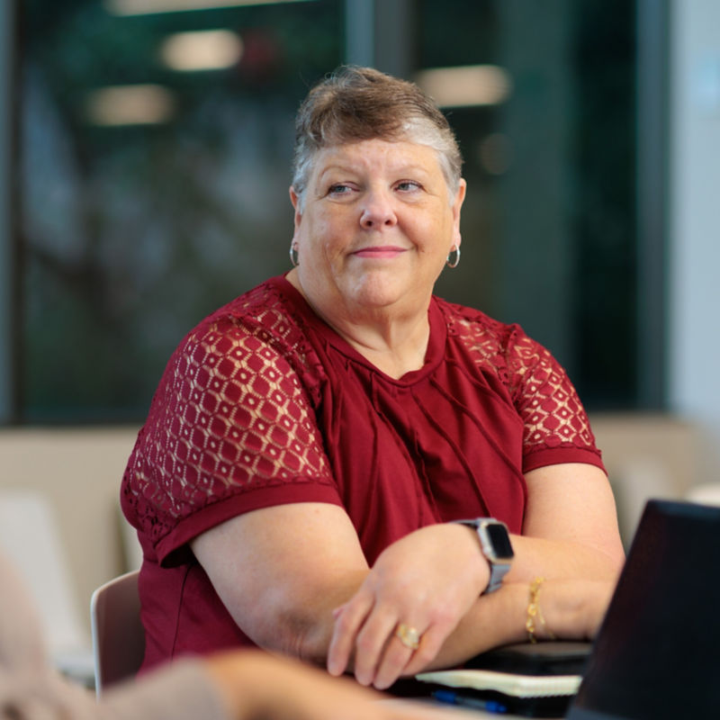a woman in a red shirt sitting at a table with a laptop