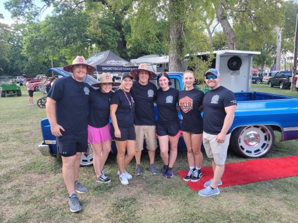 A group of seven people, including Terry Hill, stand in front of a blue 1897 Chevrolet Silverado.