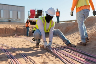 a man in a safety vest and white helmet bending over to make a line of wires