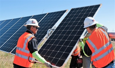 men in orange vests holding solar panels