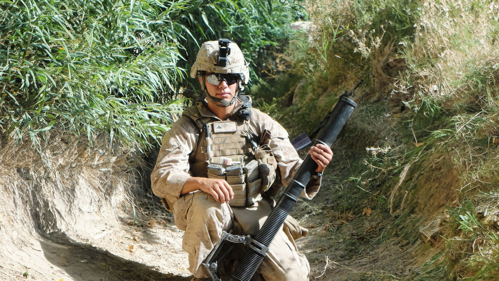 a soldier kneeling in the dirt holding a rocket