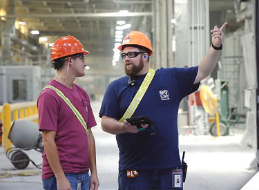 a man wearing hardhats and a blue shirt pointing at something