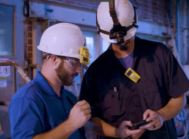 a group of men wearing hardhats and looking at a device