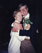 A photo of Charles Koch wearing a dark suit hugging wife Liz Koch clutching white roses in her right hand against his chest.