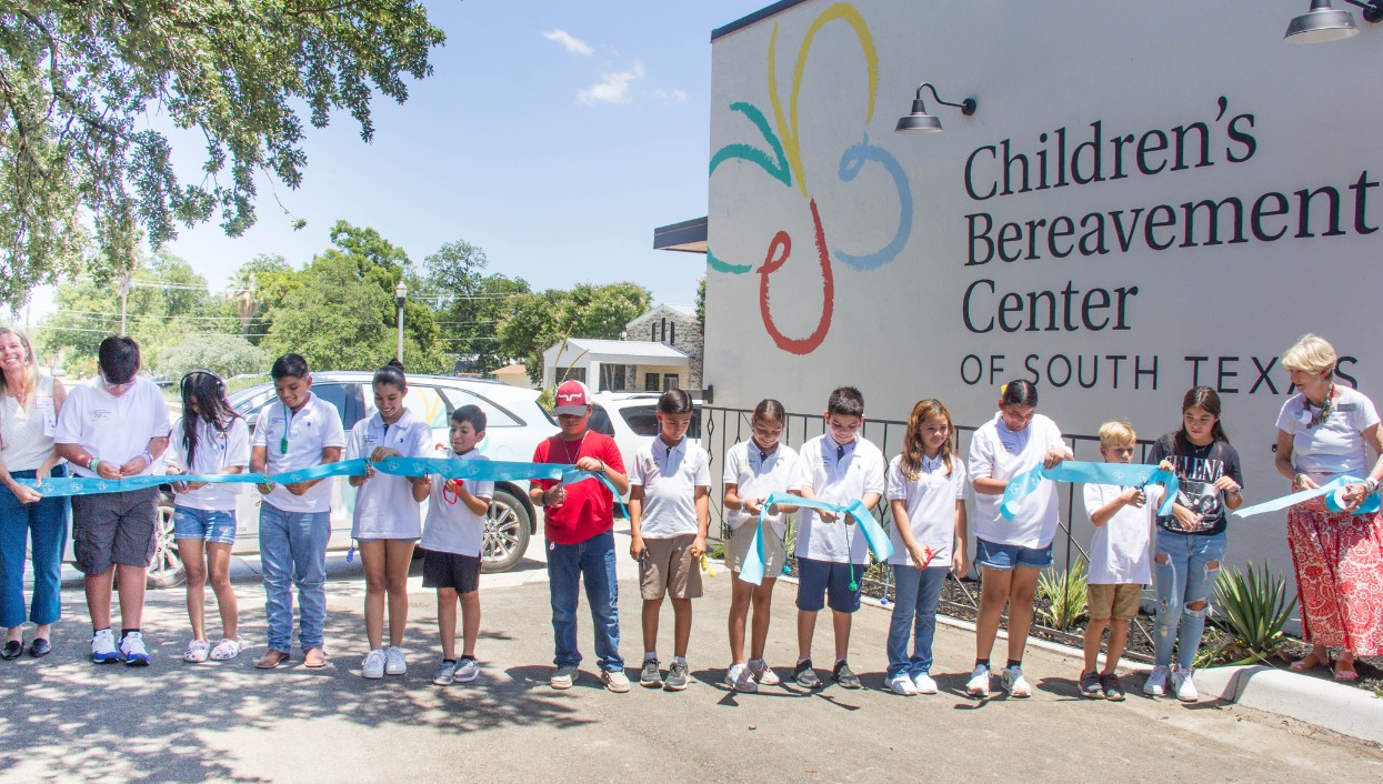 Photo of children and adults cutting a ribbon in front of the new Children’s Bereavement Center of South Texas in Uvalde, Texas. 