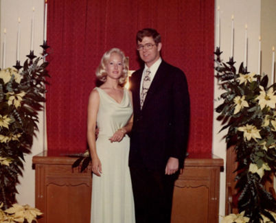 A wedding photo of Charles Koch in a dark suit and tie standing arm-in-arm with wife Liz Koch wearing a white wedding gown.
