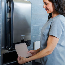 a woman putting a paper towel in a dispenser