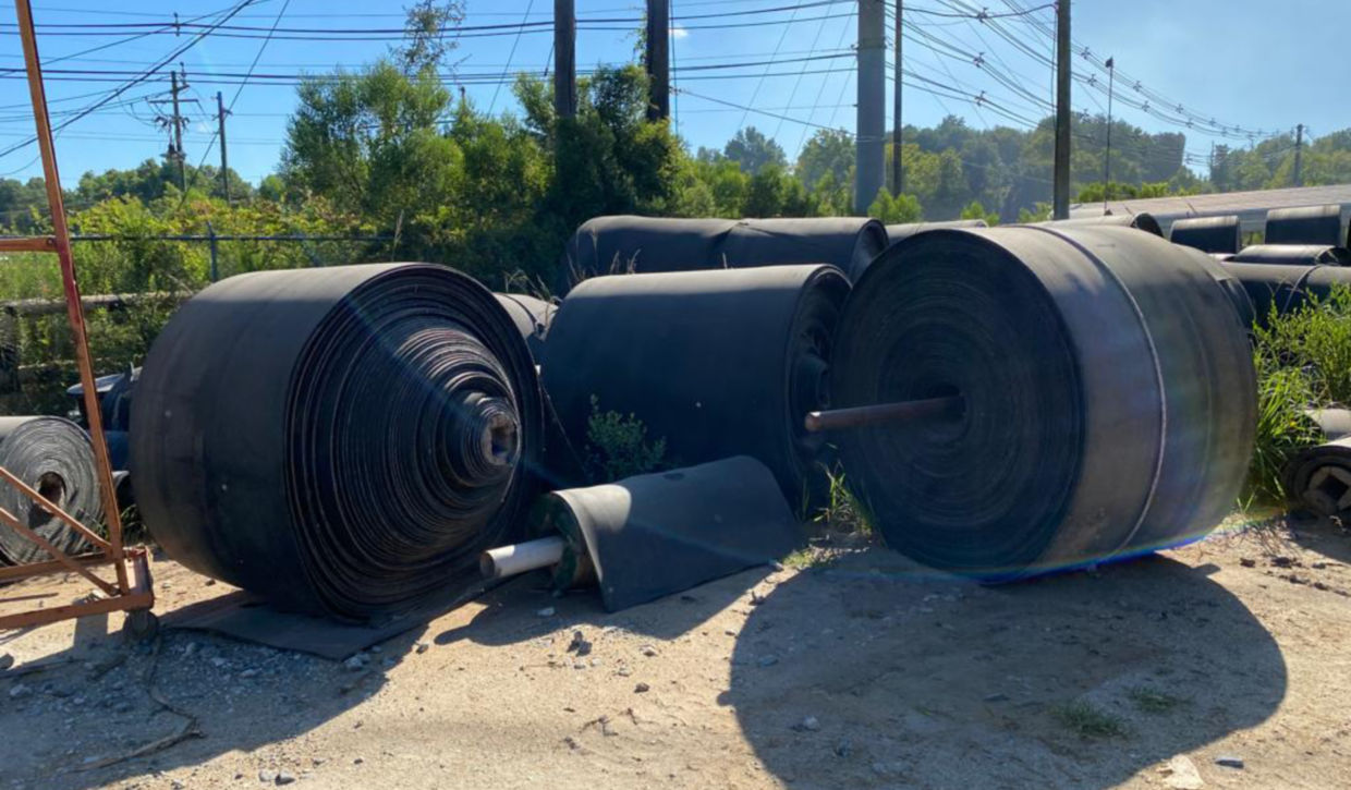 Before picture of conveyor belt rolls in Cedar Springs scrap yard before being hauled away to be recycled. 