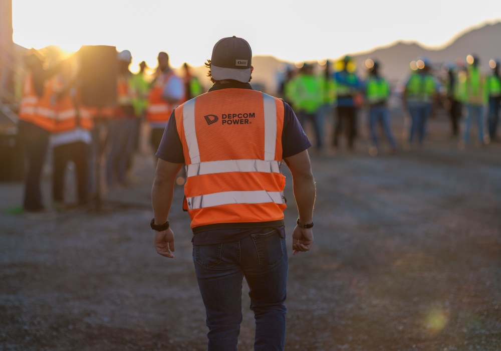 a man in a vest walking on a road with other people in the background