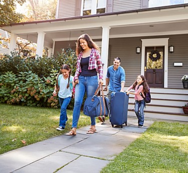 a family walking with luggage in front of a house