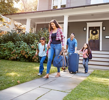 a family walking with luggage in front of a house
