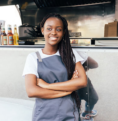 a woman wearing an apron standing in front of a food truck