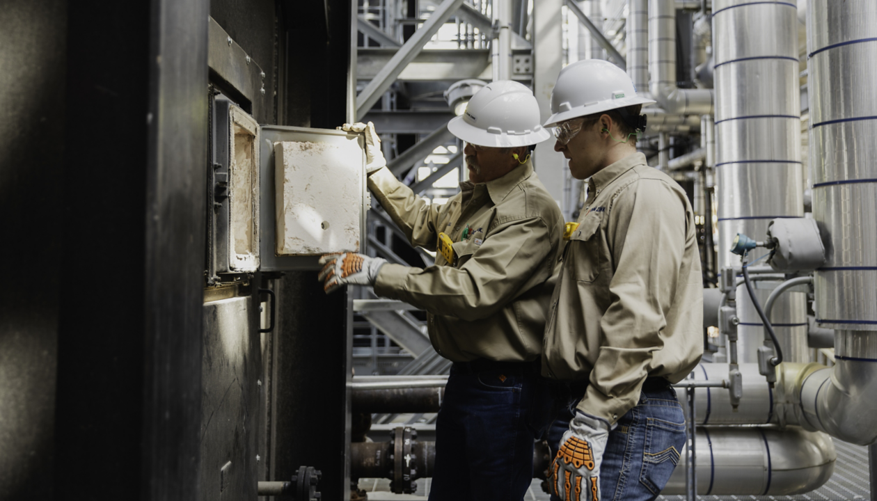 men wearing hardhats and gloves looking at a machine