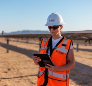 a woman in a hard hat and orange vest holding a tablet