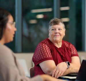 a woman in a red shirt sitting at a table with a laptop