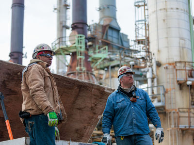 a group of men wearing hard hats and gloves standing next to a factory