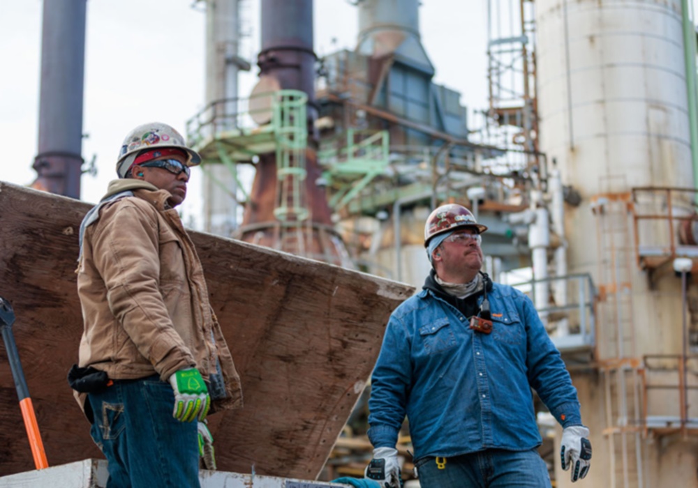 a group of men wearing hard hats and gloves standing next to a factory